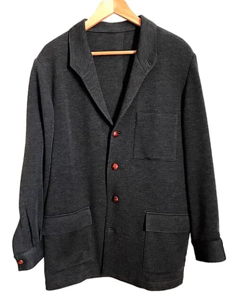 Photograph of a real charcoal Teba jacket on a hanger with three reddish buttons and flap pockets