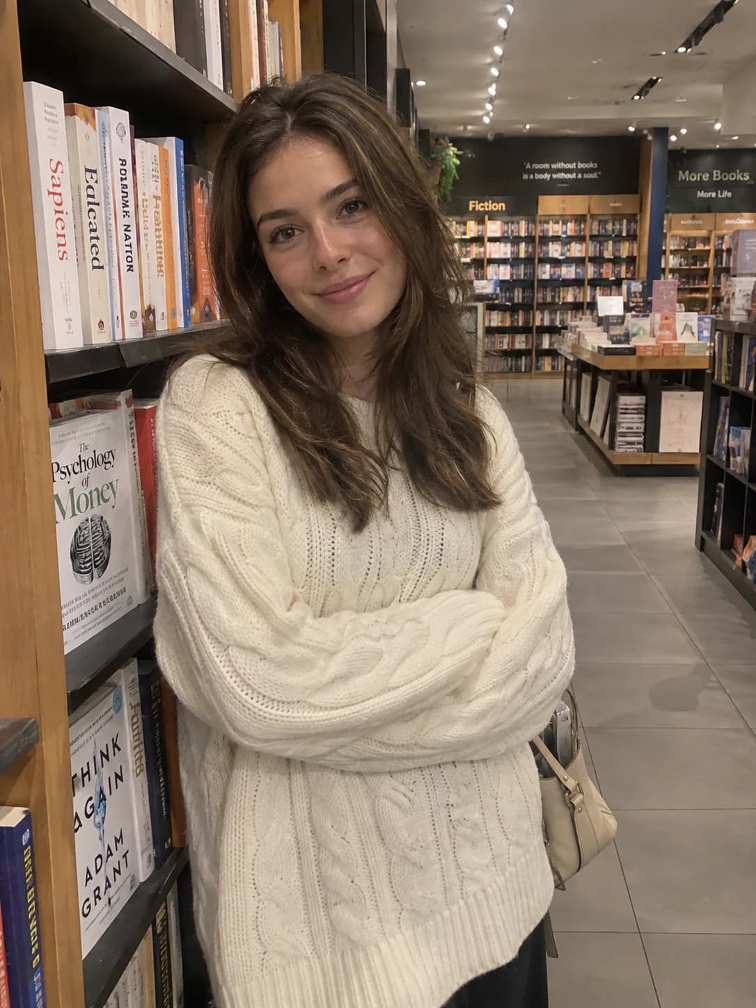 Virtual creator in a cable-knit sweater standing beside bookstore shelves