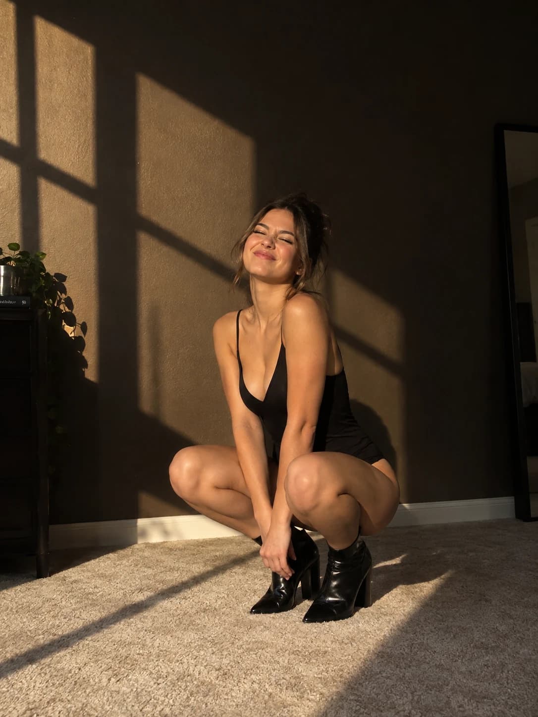 Adult virtual creator crouching in a black outfit beside geometric golden-hour window shadows