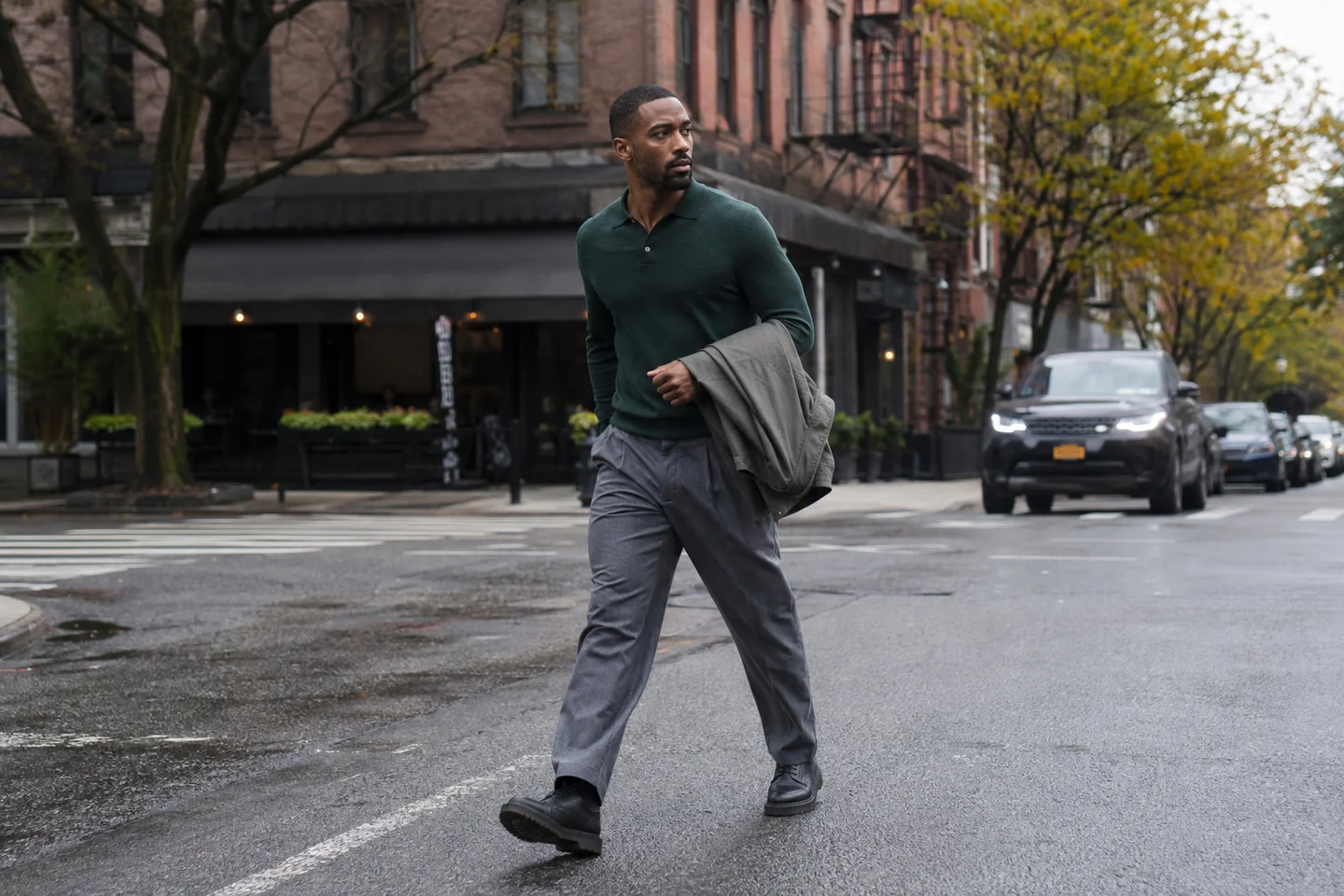 Fictional adult male fashion creator crossing a city street in a forest-green polo and gray trousers.
