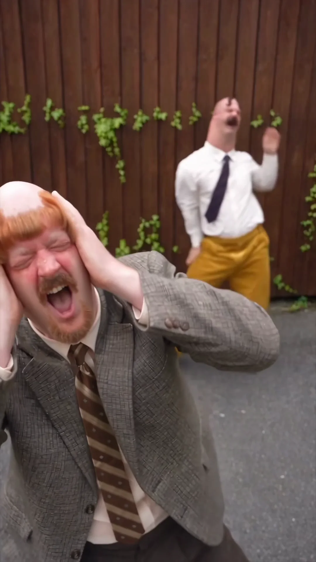 Source video at 12.2 seconds: Harold opens his mouth with both hands against his head while Madman gestures behind him