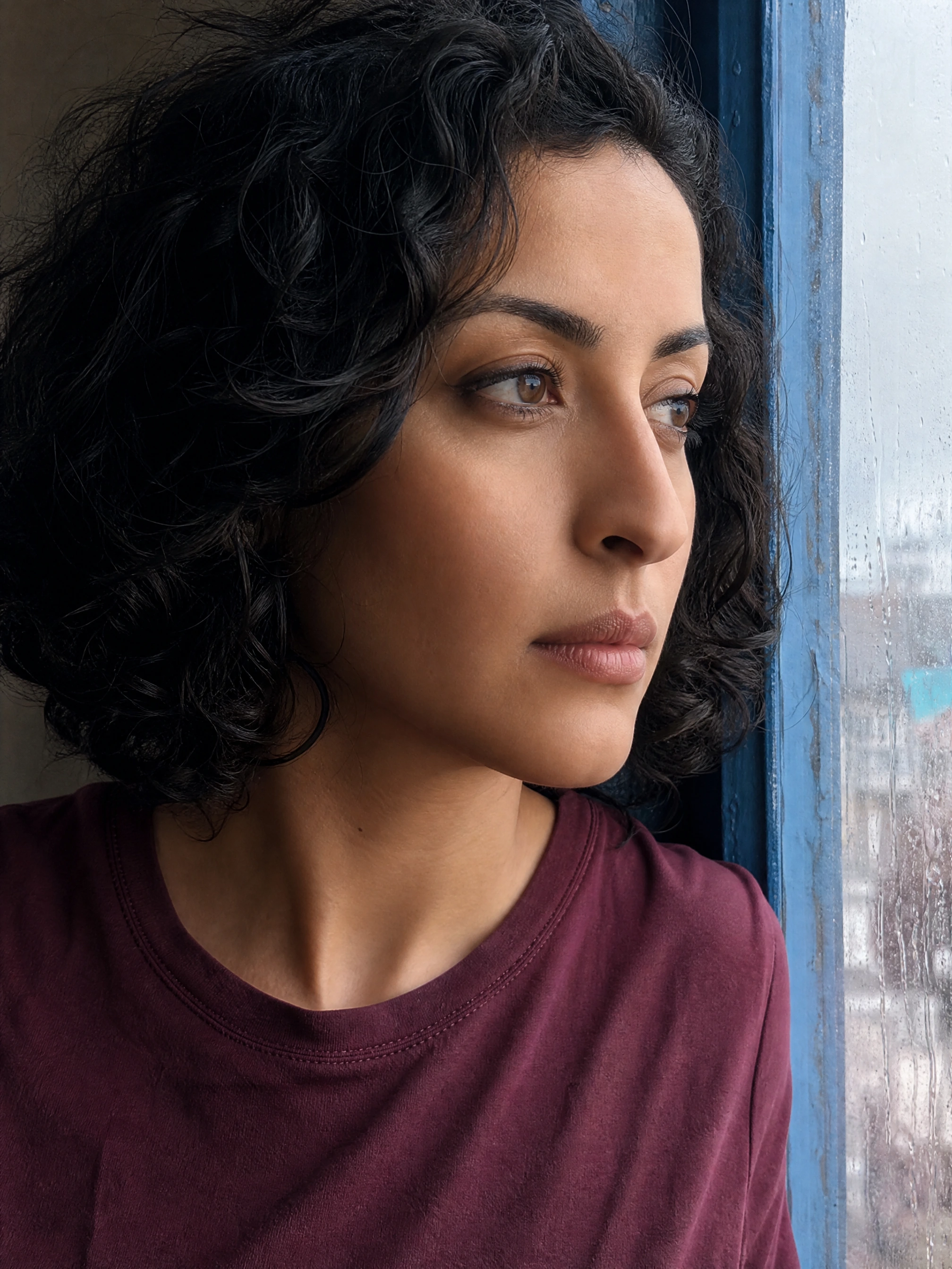 Fictional adult woman beside a rainy window, before skin texture editing