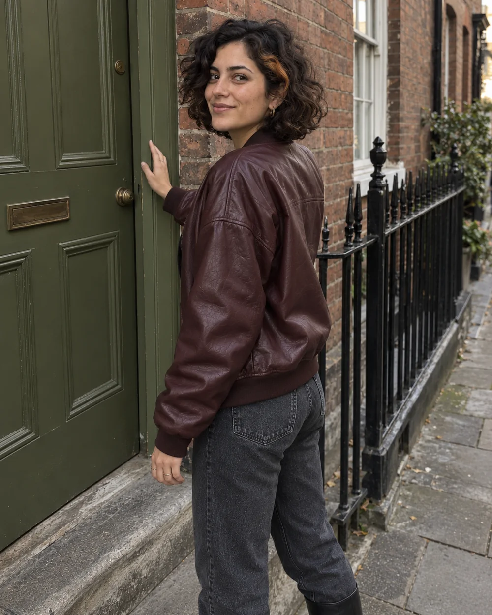 Turning back toward the camera beside the same brick doorway; the same fictional adult, outfit, and location, shot 4